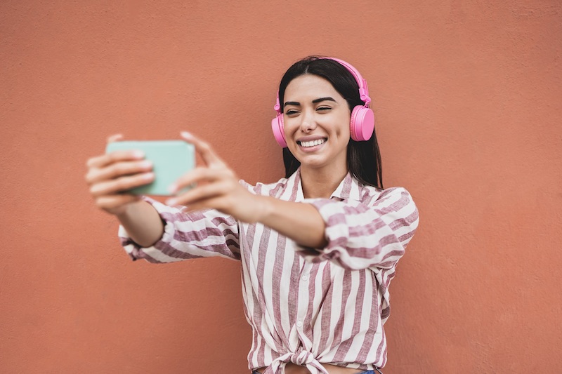 Influencer latin girl streaming live video using mobile phone while wearing wireless headphone