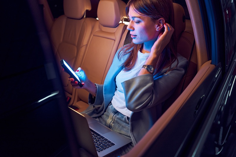 Woman using smartphone and laptop in car